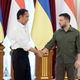 Indonesian leader Joko Widodo in a white dress shirt and black trousers shaking hands with Ukrainian president Volodymyr Zelenskyy in his trademark olive green, in front of some flags.